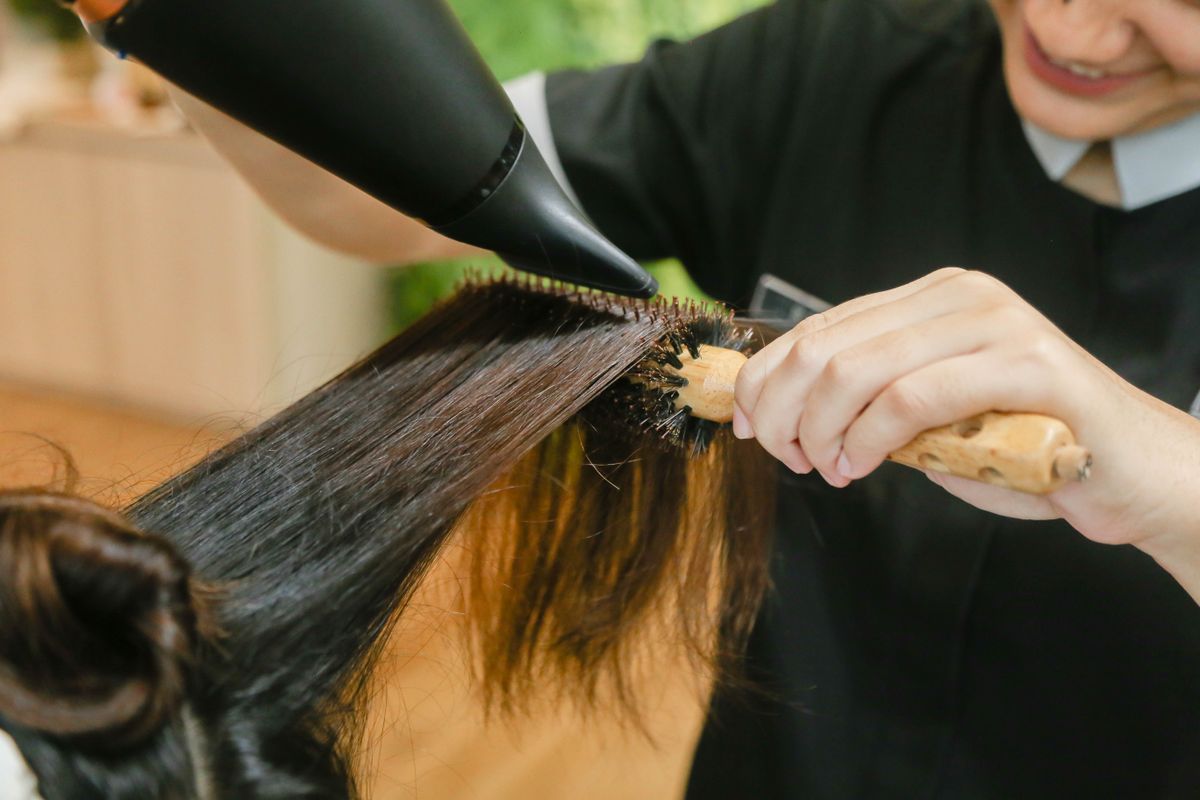 Stylist blow-drying long hair smooth